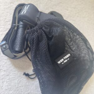 Close-up of a black mesh drawstring bag with a small label reading 'WER TREN' attached to a strap on a light concrete surface